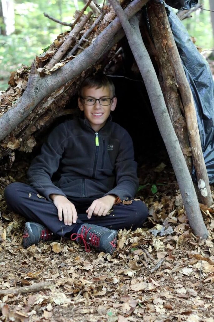 Kinder Survival Kurs: Junge sitzt in selbst gebauter Behausung